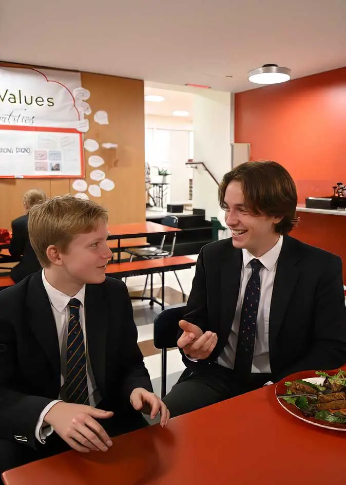 Two teenage boys having a conversation at dining hall table